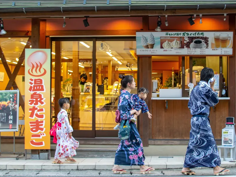 Gezin in yukata wandelt langs een winkeltje in een Japans onsendorp
